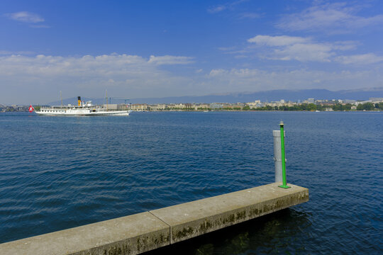 A white paddle steamer boat of CGN company moves across the calm lake, its bright flag and smokestack 