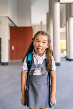 Elementary student wearing school uniform and backpack, making a playful face, ready for back to school at the corridor