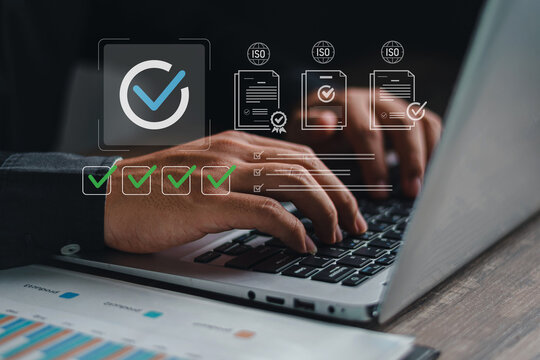 Close up of hands typing on laptop with ISO standard certification documents and green checkmark checklist icons