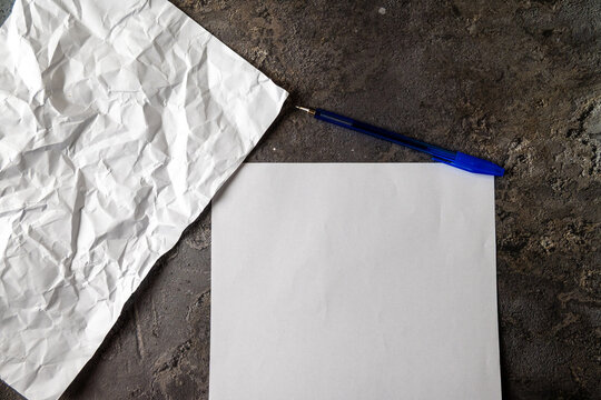 Blank Paper with Blue Pen and Crumpled Sheets on Dark Surface