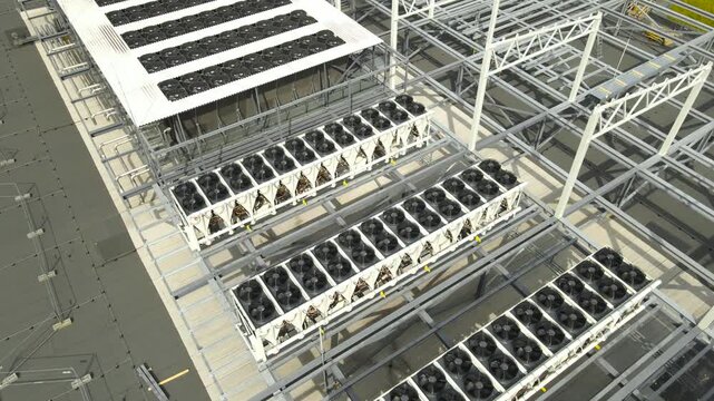 High angle view of massive industrial air conditioning units with spinning fans on the rooftop of a data center building currently under construction. Showcasing modern infrastructure and technology