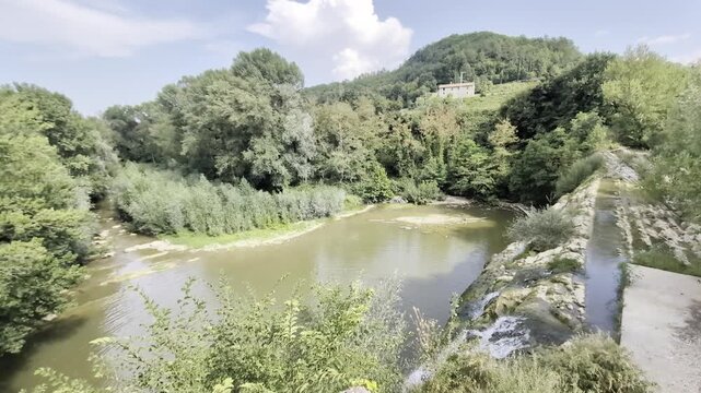Panoramica aerea del fiume Metauro e della storica diga artificiale della Cascata del Sasso, circondati dalle verdi colline di Sant'Angelo in Vado