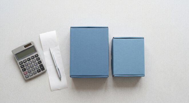 Two blue cardboard boxes with a calculator and blank receipt on a light desk