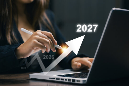 Businesswoman uses laptop and digital pen with rising arrow toward 2027, representing business growth, financial planning, strategy, success, innovation, progress, and future goals.