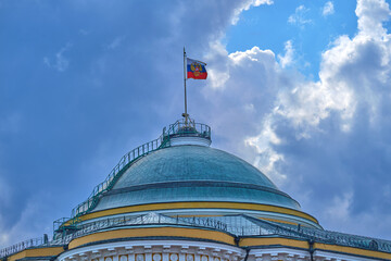 Fototapeta premium Senate Palace dome in the Moscow Kremlin with Russian flag against a dramatic blue sky. Historic government architecture and national symbol in Russia.