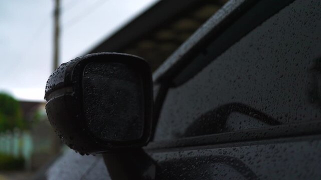 Close-up of raindrops on a dark car side mirror and body after rain. Ceramic coating effect, water repellent property, auto detailing, and rainy season weather concept. 