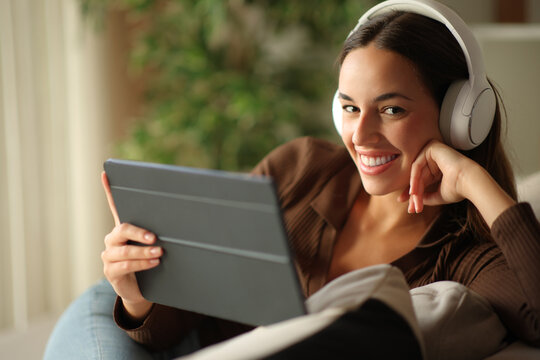 Happy woman looking at camera wearing headphone using tablet