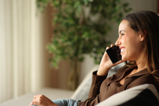 Happy woman is talking on phone at home looking away