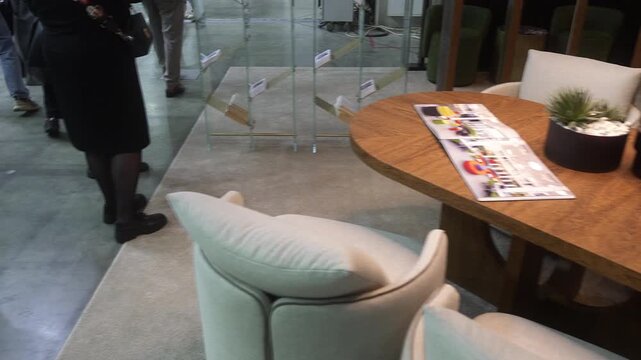 Showroom table scene with subtle chair rotation and background foot traffic, with table, wood, chair, upholstery detail, showing succulent, plant, pot, magazine context