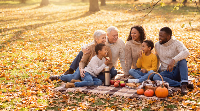 Autumn Family Picnic: A multi-generational family enjoys a warm autumn picnic on a blanket covered with fallen leaves, surrounded by trees in a park. The golden sunlight filters through the branches.