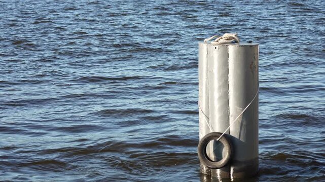 Gentle ripples dance against a solitary grey mooring bollard during a bright afternoon.