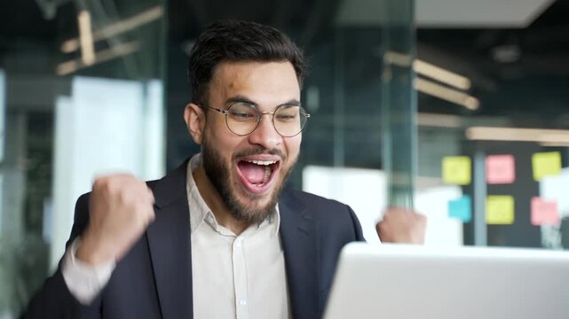 Happy excited businessman in formal suit received great news on laptop sitting at workplace in business office. Smiling shocked surprised entrepreneur reads positive good message on computer. Close up