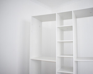 Low angle view of a newly assembled white modular wardrobe and open shelving unit installed against a white wall with crown molding in a minimalist room © Gulmira Uatkhanova