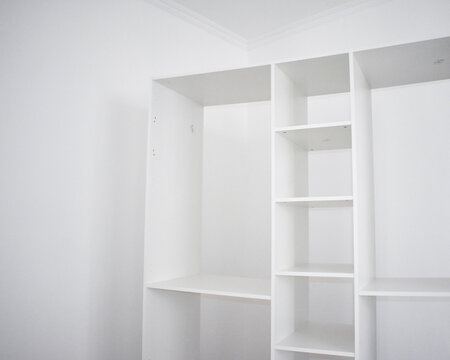 Low angle view of a newly assembled white modular wardrobe and open shelving unit installed against a white wall with crown molding in a minimalist room