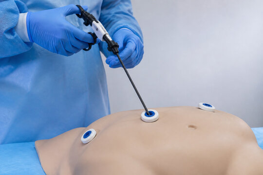 Surgeon hands positioning laparoscopic instrument on abdomen model