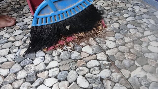 Sweeping Organic Waste and Corn Husks with Broom into Dustpan on Stone Floor