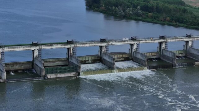 Isola Serafini Dam spans the Po River beside its hydroelectric power plant in Monticelli d'Ongina, Piacenza, Emilia-Romagna, Italy, with water flowing through spillway gates, slow slide.