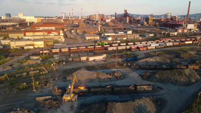 Excavator working glowing slag with flare in front of a steelworks