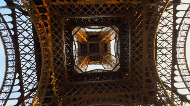 Low angle view from directly beneath the eiffel tower. The intricate iron lattice structure spinning, creating a mesmerizing abstract pattern.