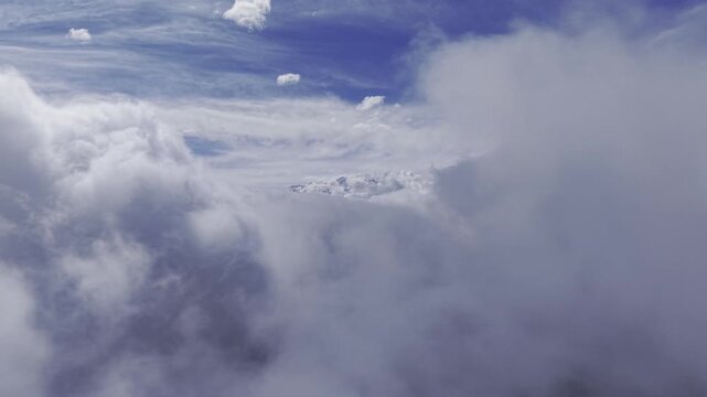 Aerial drone moves along thick rolling clouds as snow-covered Andes peaks emerge and disappear behind shifting mist under a deep blue sky. Chile, 4K