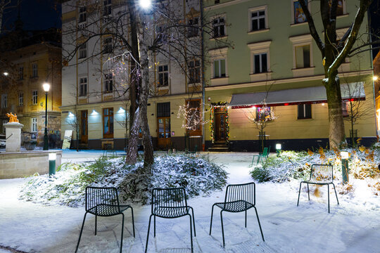 Winter evening square with snow-covered ground and empty chairs
