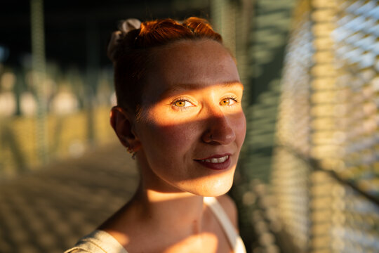 Young woman smiles with sunlight and shadow patterns on her face