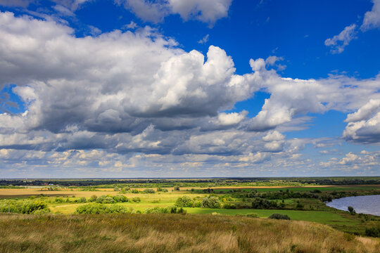 Expansive rural vista with rolling grasslands, river, and dramatic cloud cover
