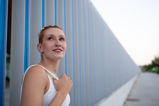 A young white woman looks thoughtfully beside a modern wall
