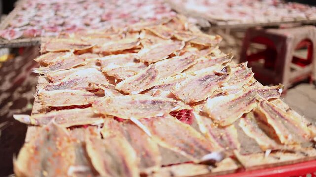 Close-up of small sun-dried fish fillets seasoned with chili spices drying on wooden racks at a local fish market near the port in Nha Trang, Vietnam. Traditional seafood processing industry, food.