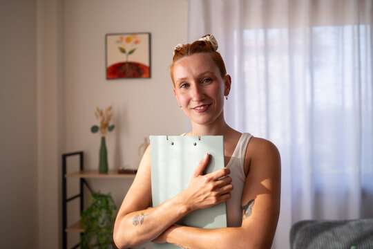 A smiling white woman holds a folder in a bright home office setting