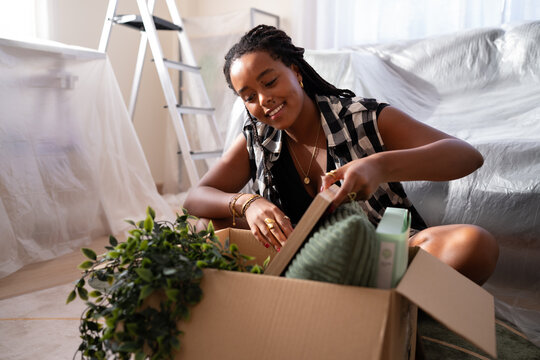A African American woman unpacks home items in a room while moving
