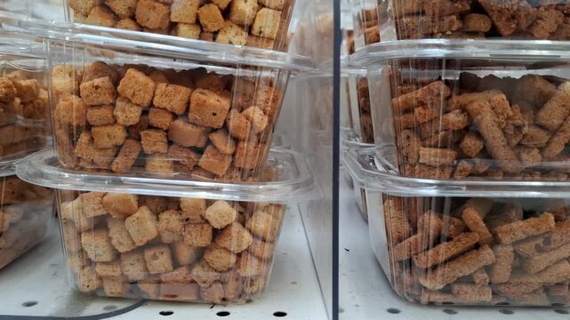 Brown bread croutons displayed in clear containers at a food market, bakery ingredient, snack, texture, retail, and food preparation.