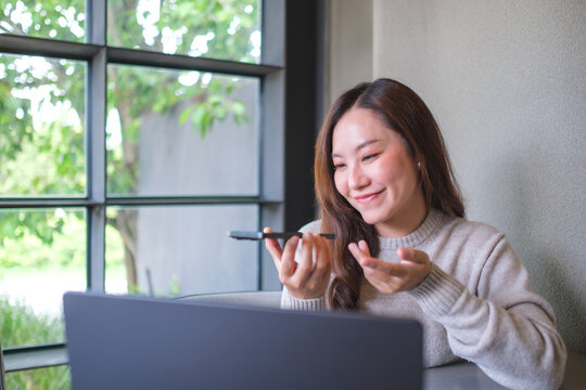 A woman holding smart phone and using voice messaging, talking with ai assistant for Artificial intelligence concept while working on laptop