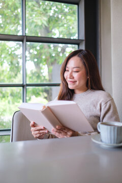 Vertical portrait image of a woman reading a book with coffee cup on the table