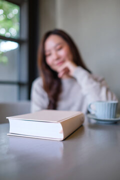 Vertical blurred image of a woman with a book and coffee cup on the table