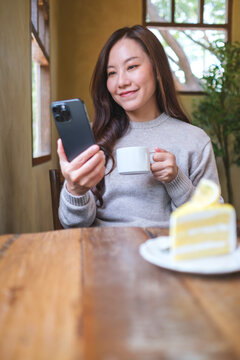 Vertical portrait of a woman holding mobile phone while drinking coffee in cafe