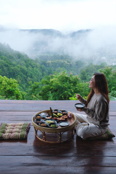 A woman eating breakfast on Northern Thai traditional dining table while looking at foggy mountain views