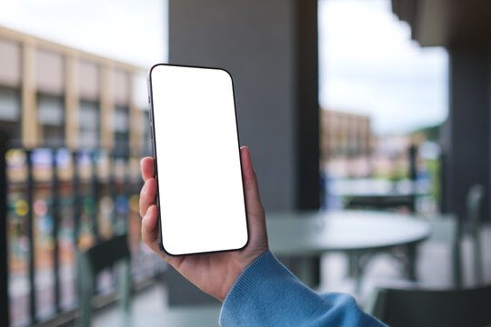 Mockup image of a woman holding and using mobile phone with blank desktop screen in cafe