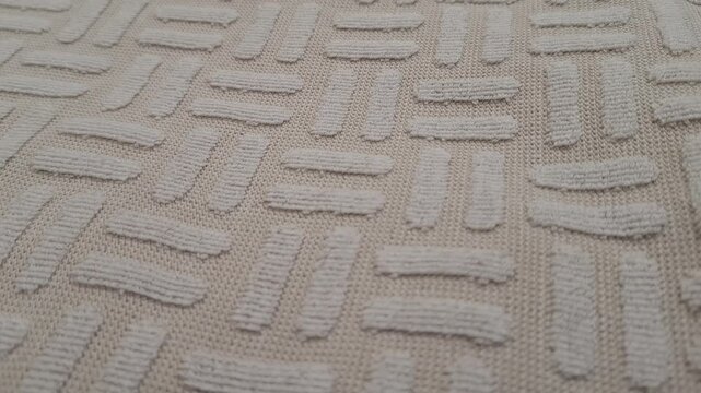 Close view of a textured beige rug with raised geometric patterns, interior decor detail, cozy home styling, neutral design, and modern comfort.