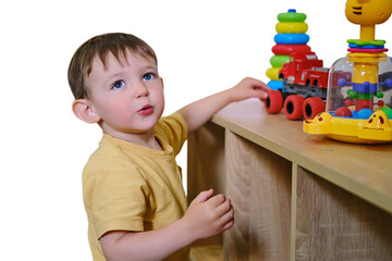 Fototapeta na wymiar Child boy playing with educational toys on wooden shelf. Toddler standing at home learning to play with colorful stacker and transport models. Early development and daycare concept.