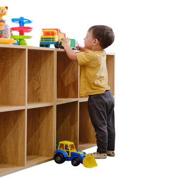 Toddler boy playing with toy truck on wooden shelf. Child reaching for plastic vehicle toy. Developmental play and activity at home. Educational games for toddler boy in kindergarten.