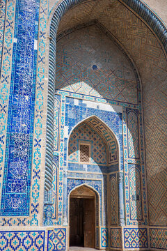 Detailed view of historic Islamic architecture in Uzbekistan featuring a monumental pointed arch decorated with intricate blue and turquoise tilework, Arabic calligraphy, geometric patterns