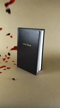 Shiny red heart shaped confetti falling in slow motion on a closed black Holy Bible. The religious concept represents God's love, faith, and the scripture as a source of divine affection