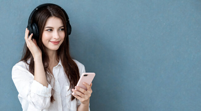 Young woman listens to music with headphones while holding a smartphone in a simple indoor setting