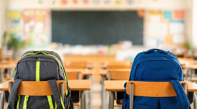 Two backpacks sit on classroom chairs in a school during a lesson