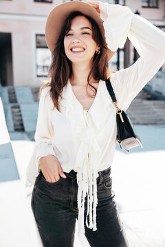Portrait of young beautiful smiling hipster woman in trendy summer white blouse and jeans. Carefree woman posing in the street in sunny day. Positive model outdoors. Cheerful and happy