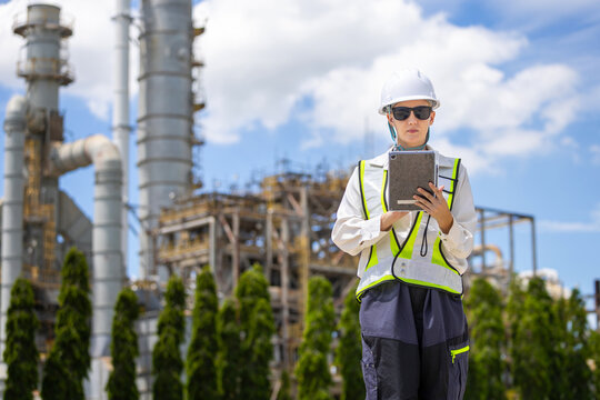 Female engineer with digital tablet inspecting oil refinery plant, woman worker in hardhat and safety vest checking petroleum refinery facility
