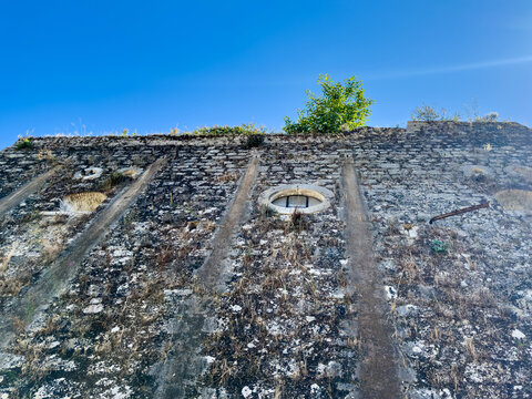 Weathered stone wall with round openings under blue sky at New Fortress, Corfu Town, Greece
