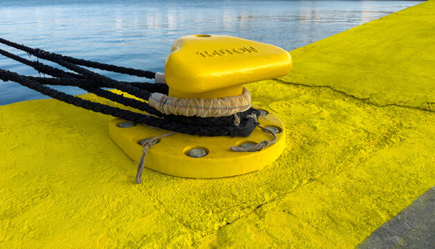 Black mooring ropes around yellow bollard on Chios harbor quay beside calm water