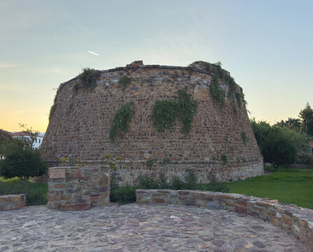 Massive weathered stone bastion draped in greenery at sunset in Chios Town, Greece